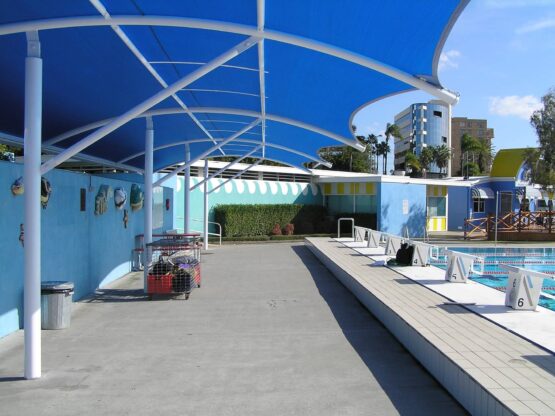 A custom shade structure beside a public pool, using blue Driz waterproof shade fabric