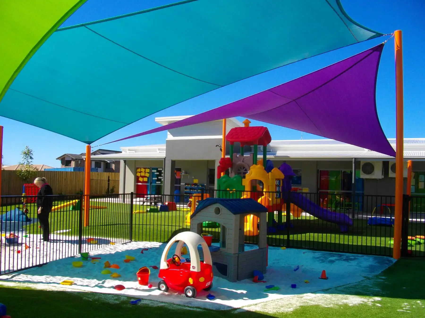 Colourful shade sails using Rainbow Shade NZ Driz fabric installed over a childcare playground at Coomera Learning Centre, providing UV protection and cool shade for outdoor play equipment and sandpit area