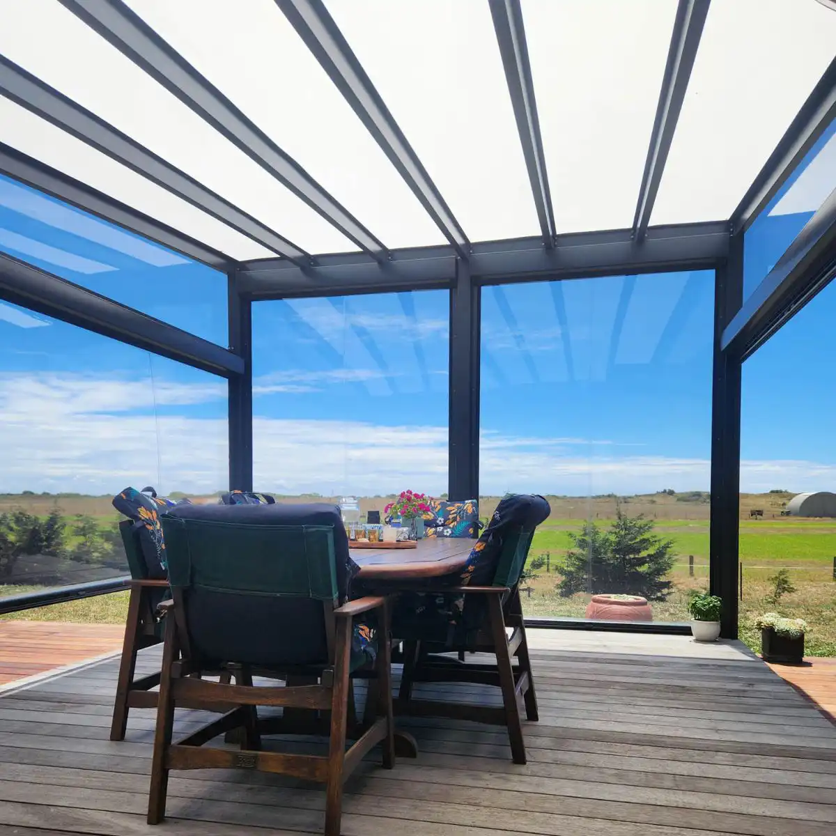 Enclosed outdoor dining area with clear PVC Ziptrak® blinds and Clearspan glazed roof systems overlooking rural New Zealand landscape