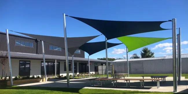 Porangahau School courtyard with modern black, grey, and green outdoor shade sails using Rainbow Shade NZ - Extreme32 covering outdoor, seating and picnic tables, under a clear blue sky