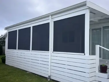 Stylish white exterior with outdoor living blinds installed along deck, featuring mesh outdoor blinds in Visiontex® Plus 94 Graphite with white Ziptrak® blinds, a modern outdoor blinds solution from Rainbow Shade NZ.